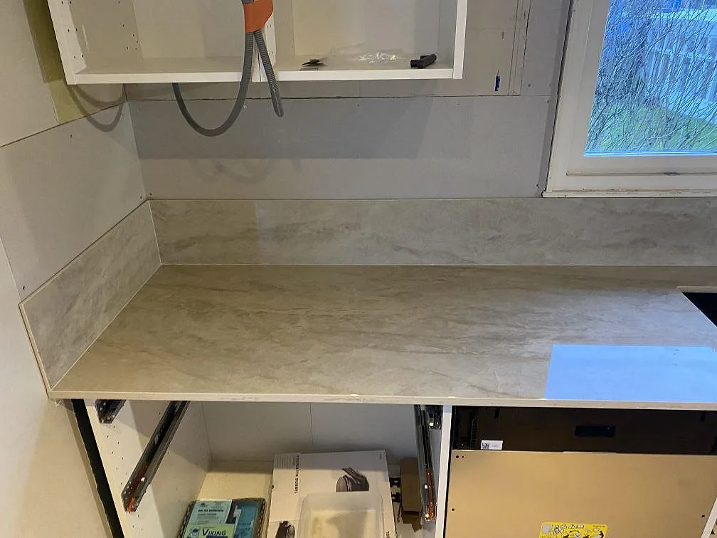 Rak köksbänk i polerad Dekton Arga med uppvikt stänkskydd och ljus beigegrå ådring i ett kök i Färlöv.