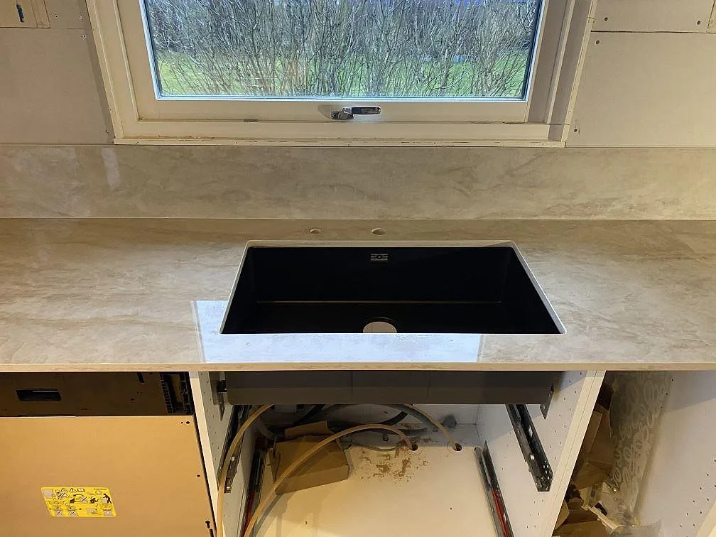 Köksbänkskiva i polerad Dekton Arga med matchande stänkskydd och svart diskho framför fönster i Färlöv.