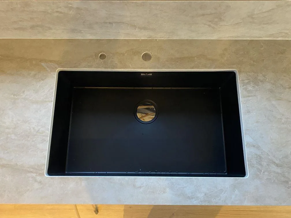Närbild på svart diskho i en polerad Dekton Arga köksbänkskiva med två runda hål och stänkskydd i Färlöv.