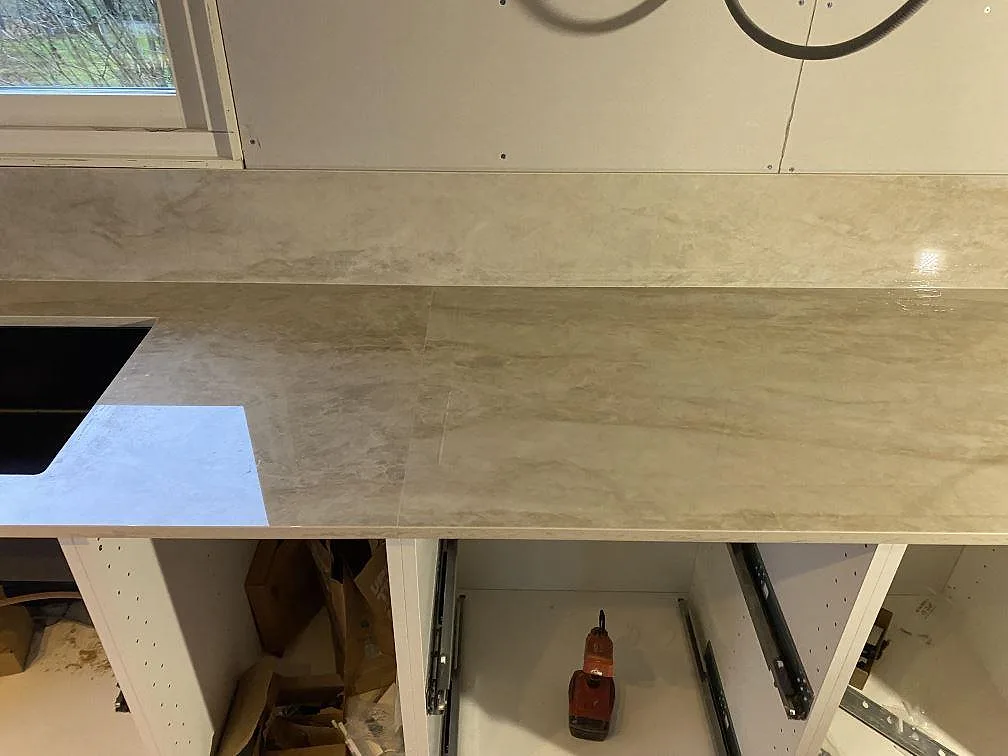 Detalj av polerad Dekton Arga bänkskiva och uppvikt stänkskydd med ljus ådring under köksmontering i Färlöv.