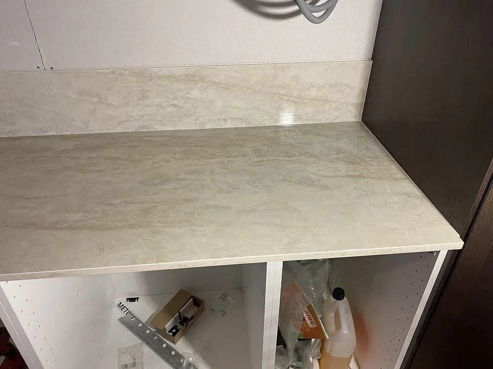 Hörnparti av köksbänkskiva i polerad Dekton Arga med matchande stänkskydd och beigegrå ådring i Färlöv.