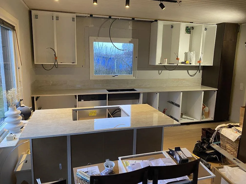 Köksbänkskiva och köksö i polerad Dekton Arga med matchande stänkskydd under montering i ett kök i Färlöv.