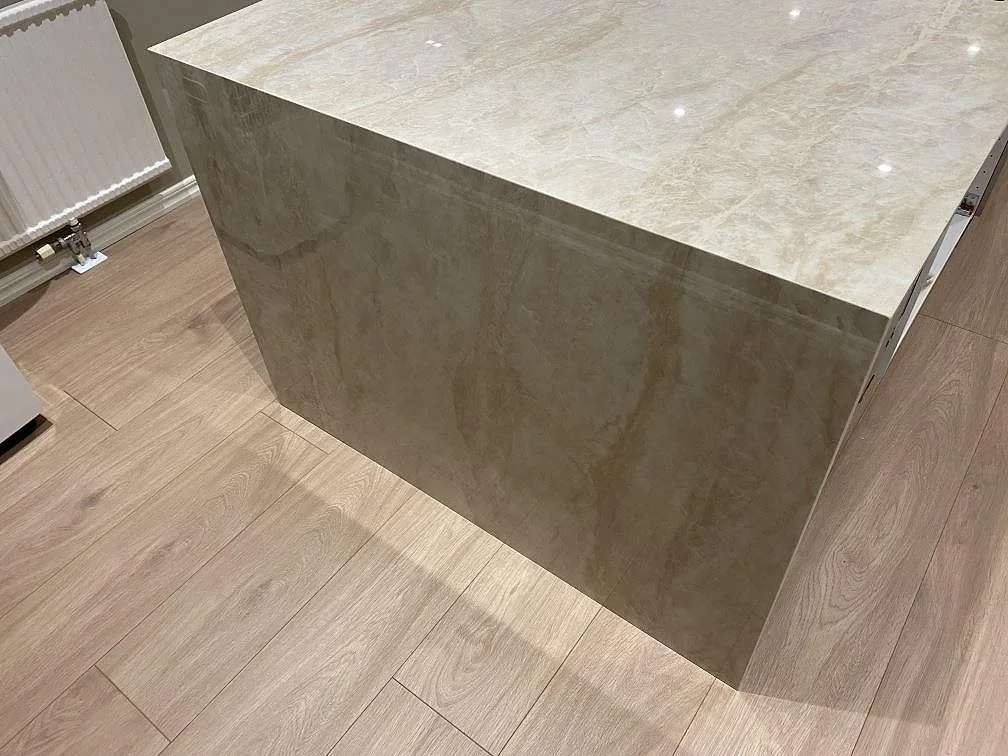 Sidovy av stenklädd gavel i polerad Dekton Arga med ljus ådring på en lång köksö i Fjärås.