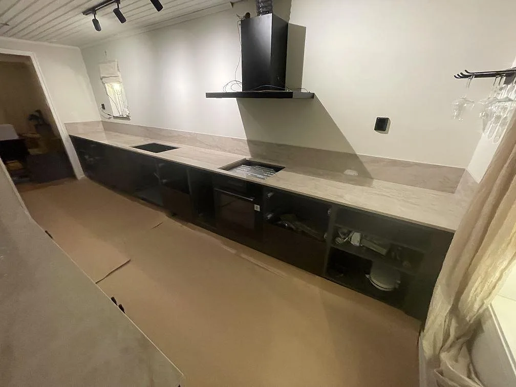Lång köksbänk i polerad Dekton Arga med urtag för diskho och häll mot svarta köksluckor i ett kök i Flen.