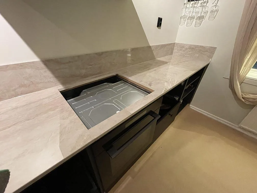 Urtag för induktionshäll i polerad Dekton Arga keramikbänk med skyddsfilm under montering i ett kök i Flen.
