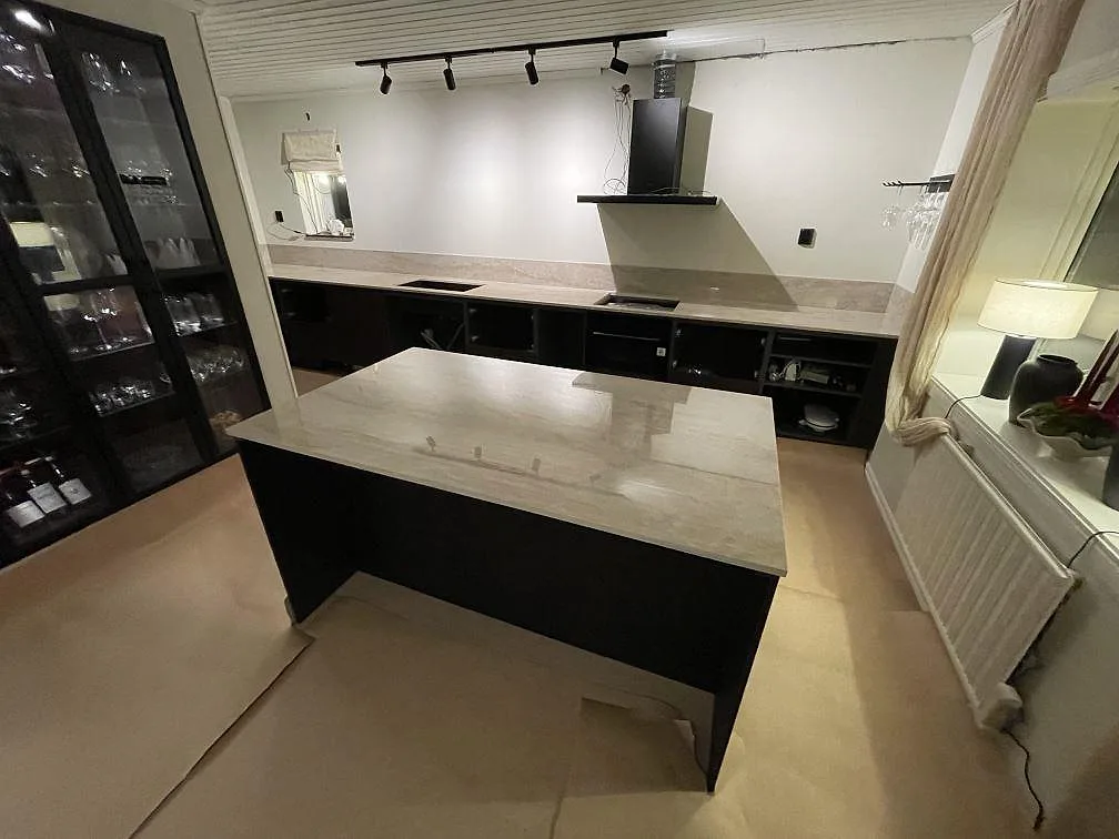 Kök i Flen med köksö och väggbänk i polerad Dekton Arga, svart stomme, frihängande köksfläkt och låg stänkkant i samma keramik.
