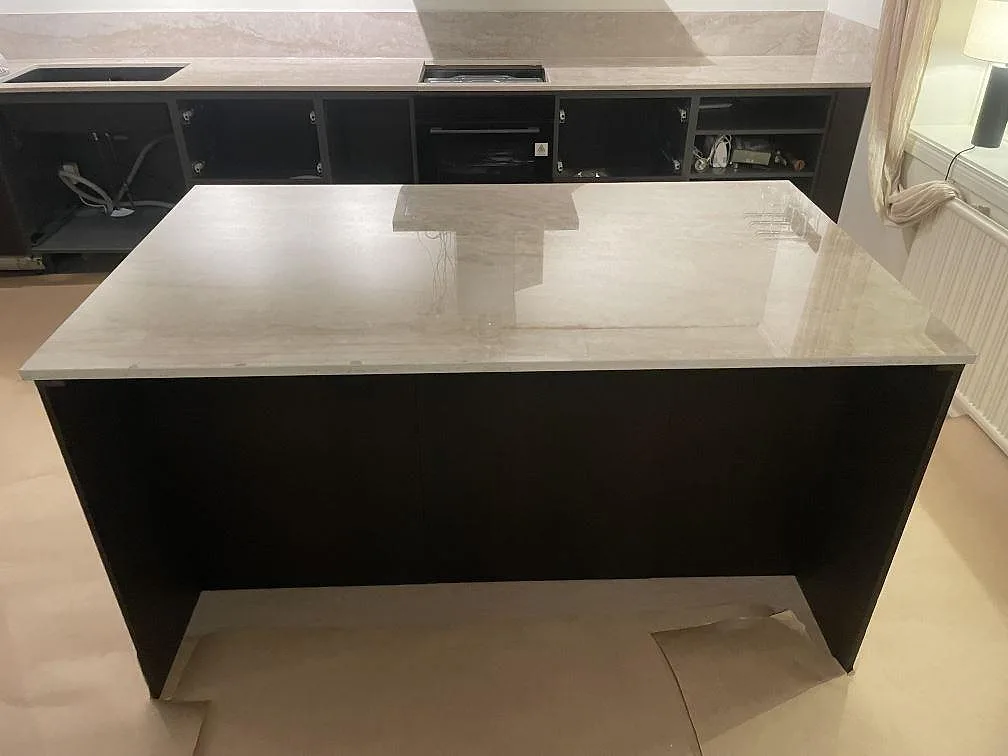 Fristående köksö i cremebeige Dekton Arga, polerad keramik med brun-guldig ådring, framför en svart köksstomme i ett kök i Flen.