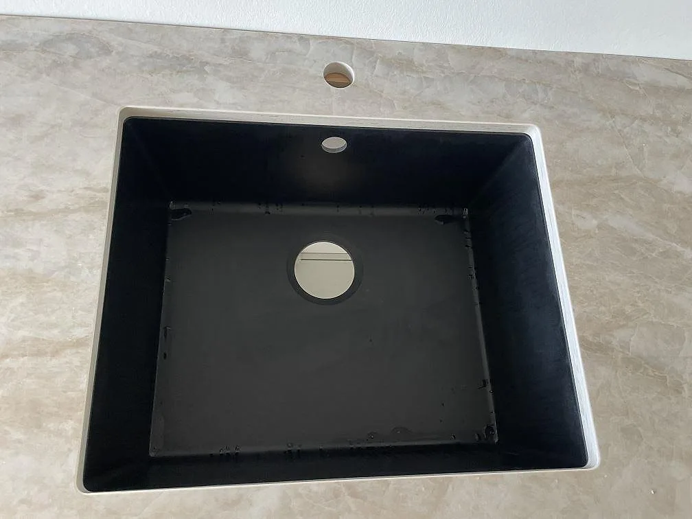 Närbild på svart diskho monterad under en polerad Dekton Arga bänkskiva med tapphål i Frederiksberg.