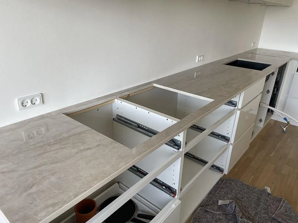 L-formad köksbänkskiva i polerad Dekton Arga keramik med hälluttag och svart diskho i ett kök i Frederiksberg.