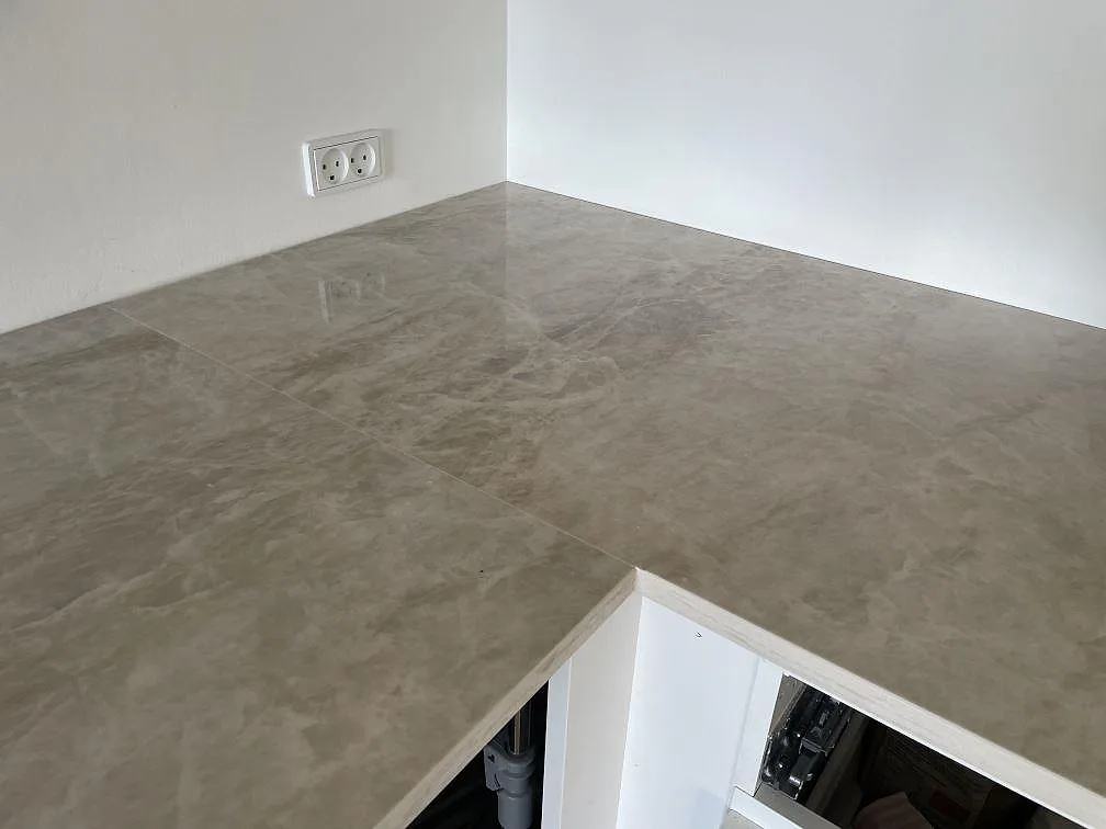 Hörnsektion av L-formad köksbänkskiva i polerad Dekton Arga keramik med reflekterande yta i Frederiksberg.