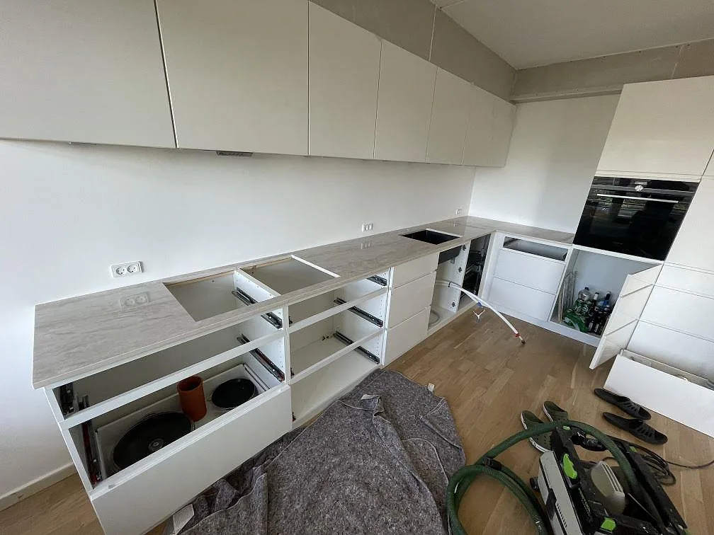 Bred köksvy med polerad Dekton Arga bänkskiva, vita köksstommar, hälluttag och underlimmad svart diskho i Frederiksberg.