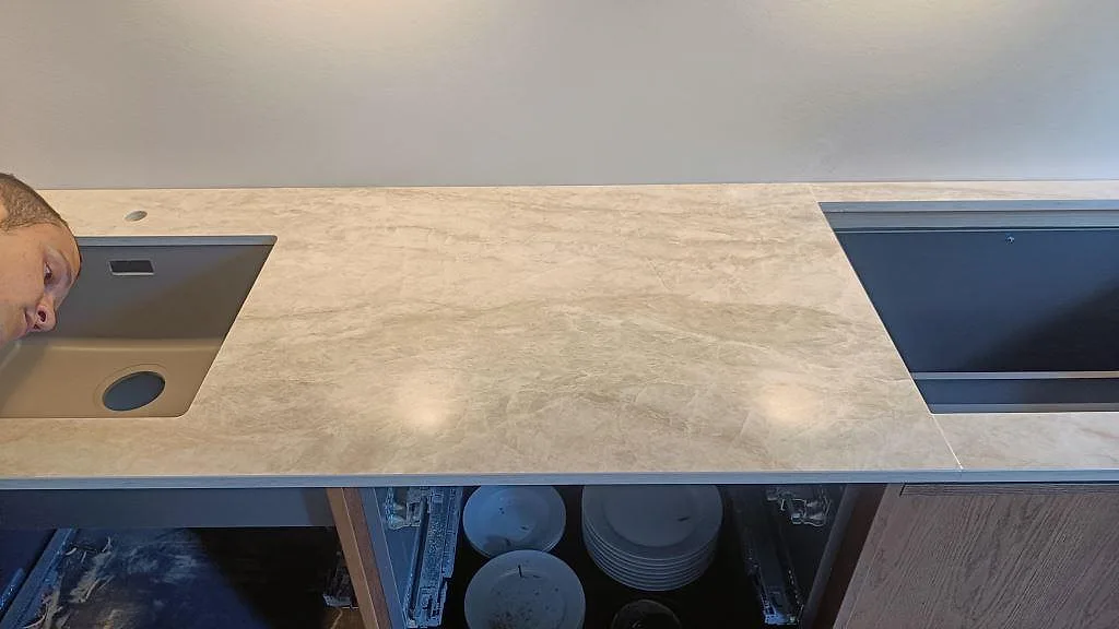 Halvö med köksbänkskiva i polerad Dekton Arga, svart häll och gråbeige ådring under montering i Frederiksberg.