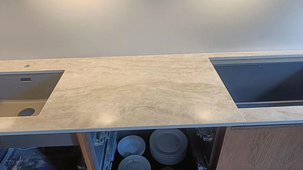 Rak bänkskiva i polerad Dekton Arga med låg stänkkant, vägguttag och vit köksstomme i Frederiksberg.