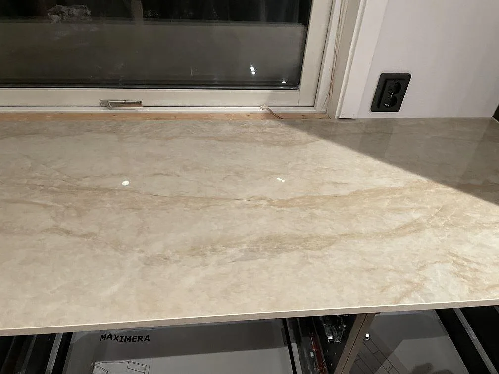 Bänkskiva i polerad Dekton Arga längs fönstervägg med eluttag i ett kök under montering i Frillesås.