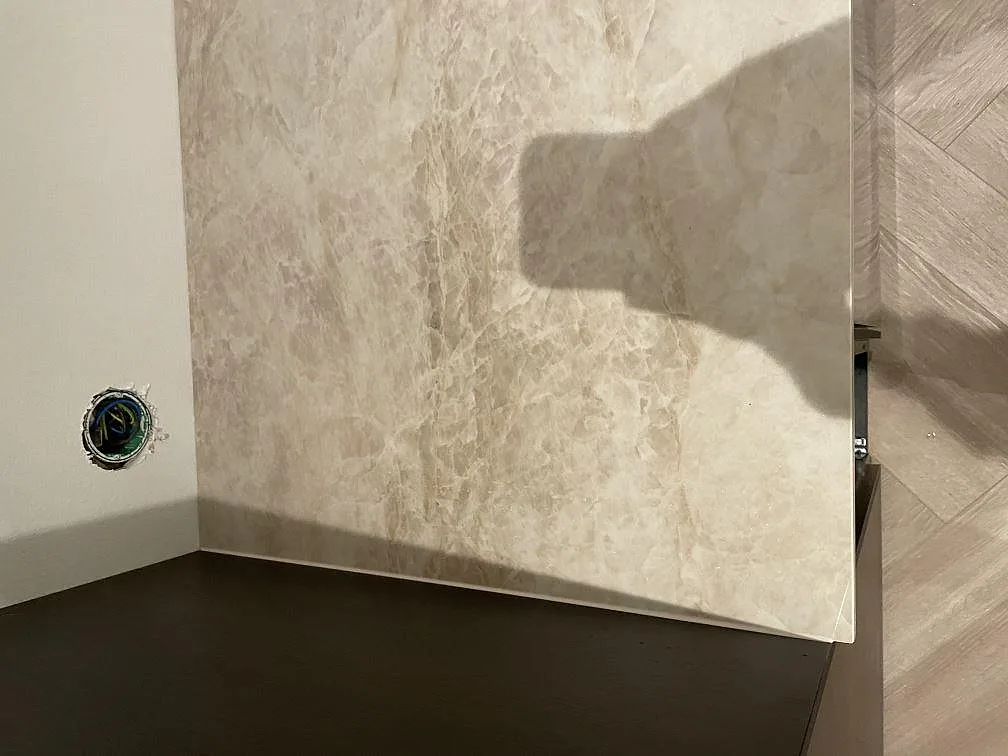 Uppvikt stänkskydd i Dekton Arga keramik mot vägg i ett kök under montering i Frillesås.