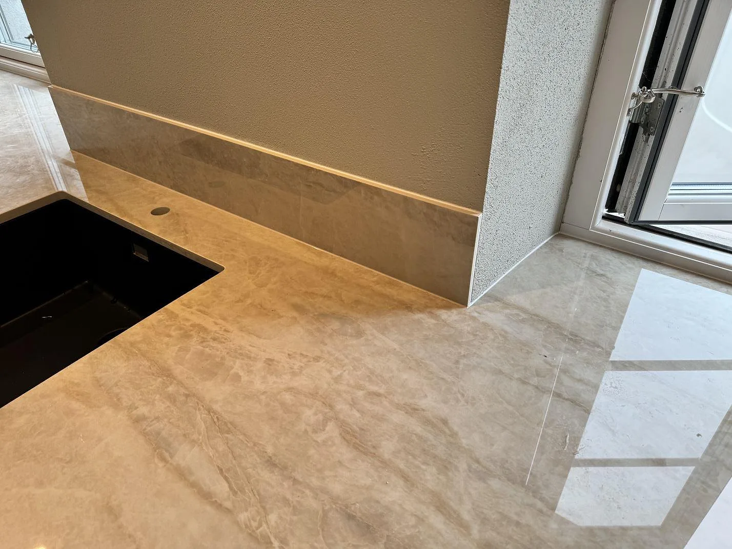 Köksbänkskiva i polerad Dekton Arga med svart diskho, stänkskydd och fönsterljus i Gärsnäs.