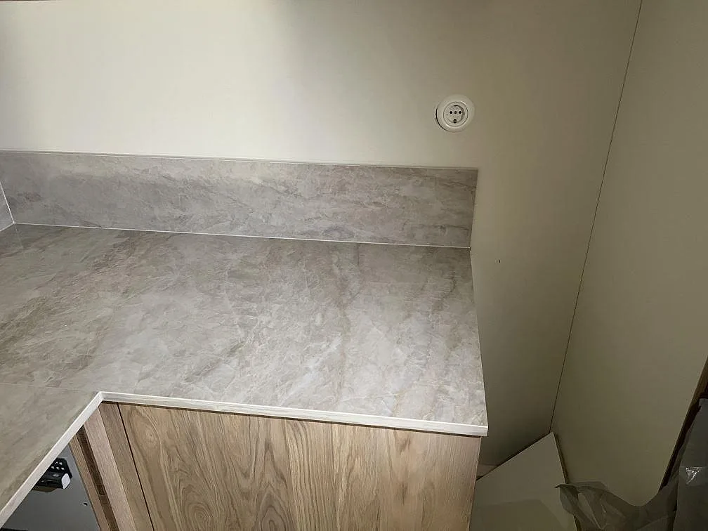 Polerad köksbänkskiva i Dekton Arga med 8 mm stänkskydd och träfronter under montering i Gemla.