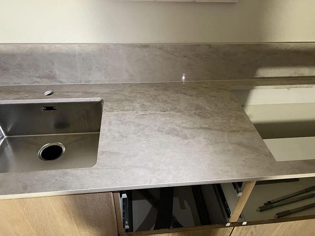 Köksbänkskiva i polerad Dekton Arga med underlimmad rostfri diskho och lågt stänkskydd i ett kök i Gemla.