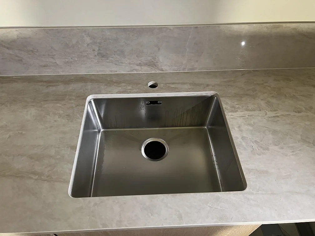 Närbild på underlimmad rostfri diskho i polerad Dekton Arga med tapphål och stänkskydd i Gemla.
