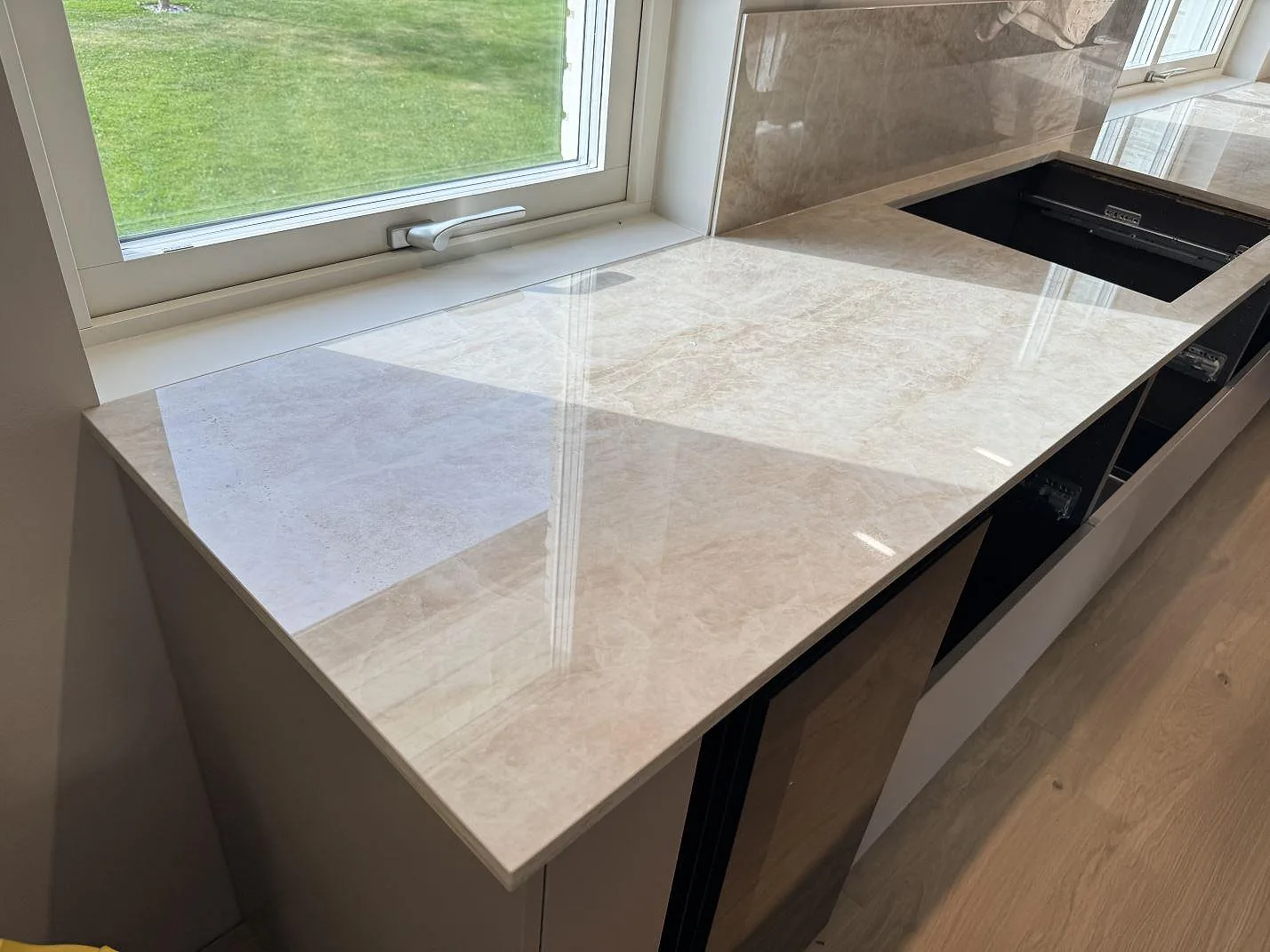 Köksbänkskiva i polerad Dekton Arga, ljus beige keramik, med fönster, stänkskydd och öppet urtag i ett kök i Gemla.