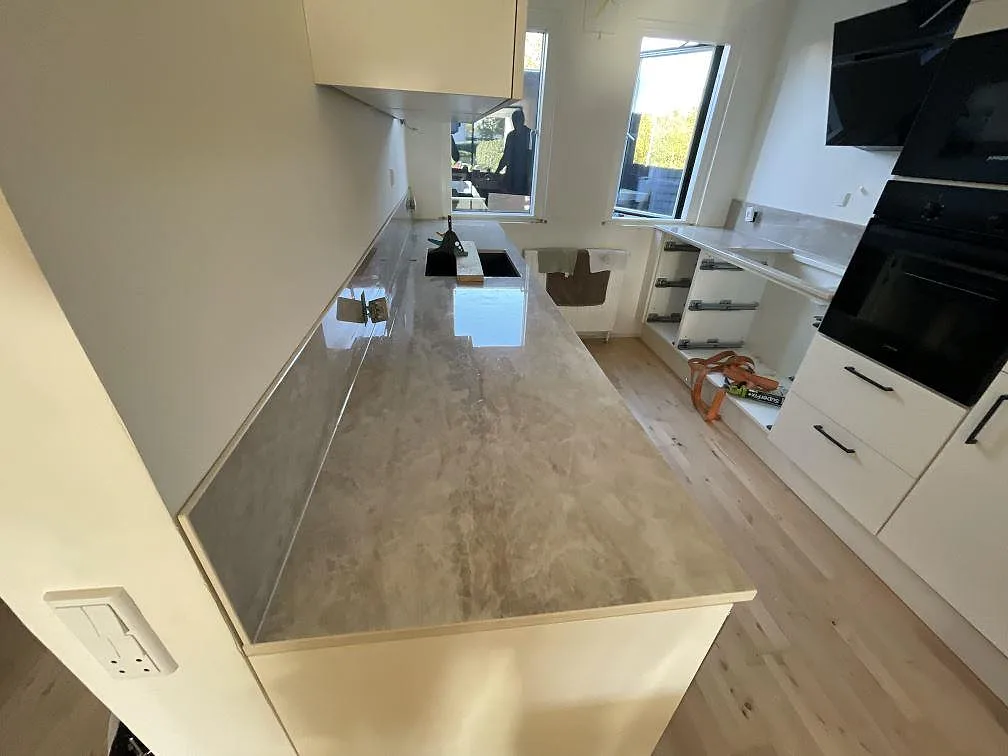 Polerad köksbänkskiva i Dekton Arga keramik med L-formad bänkrad, mörk underlimmad diskho och hälluttag i Glostrup.
