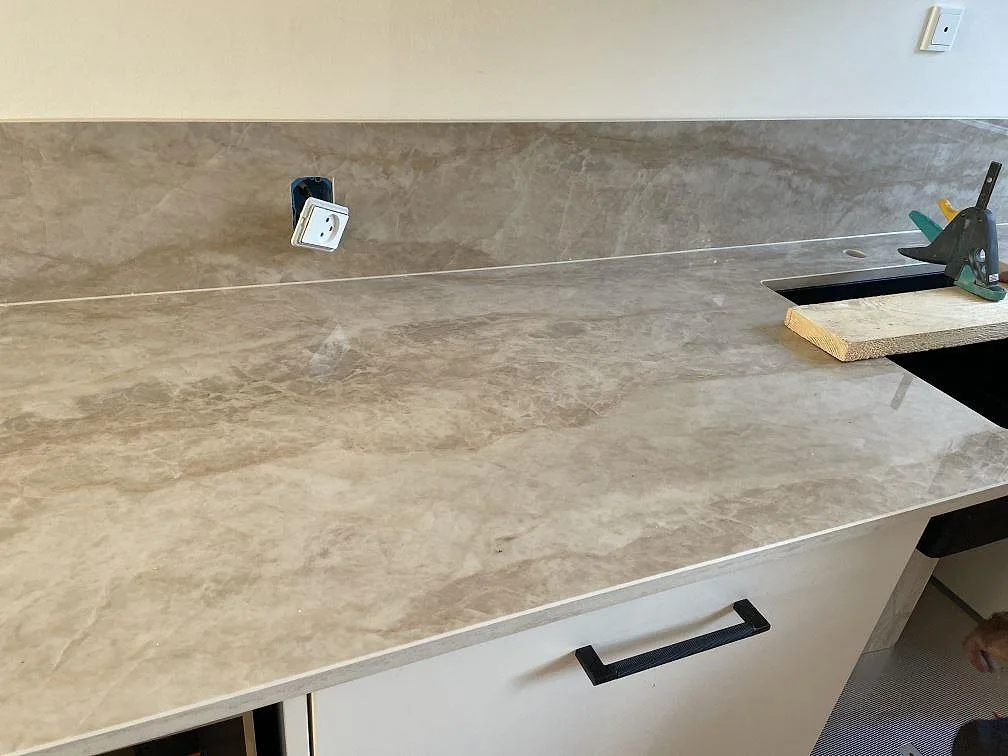 Detalj av polerad Dekton Arga keramikbänkskiva med underlimmad mörk diskho, hälluttag och väggmonterat stänkskydd i Glostrup.