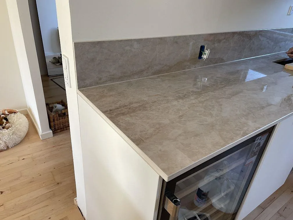 Närbild på polerad Dekton Arga köksbänkskiva i keramik med 8 mm stänkskydd och blank travertinlik ådring i Glostrup.