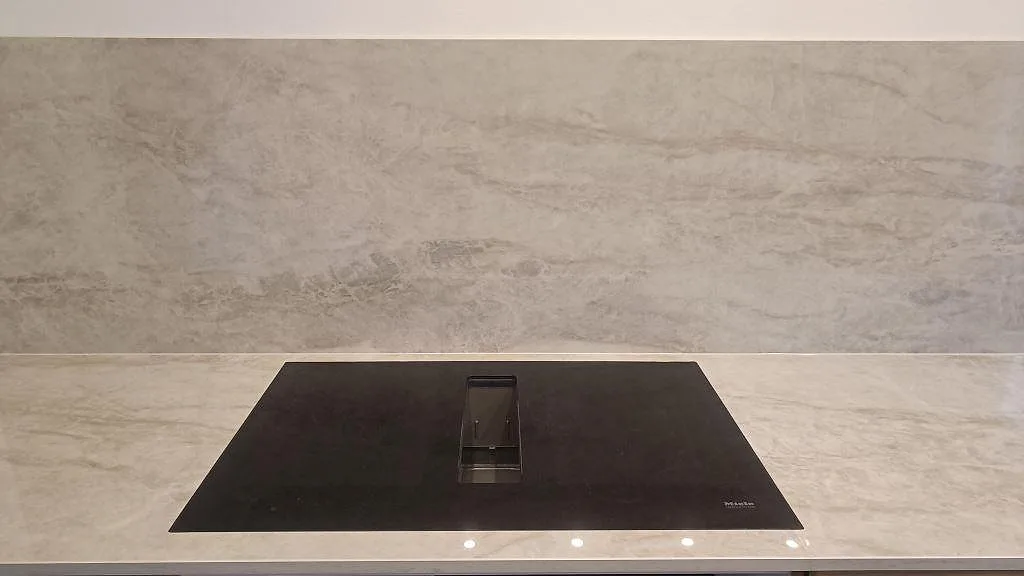 Svart induktionshäll infälld i polerad Dekton Arga med matchande stänkskydd bakom arbetsytan i Glostrup.