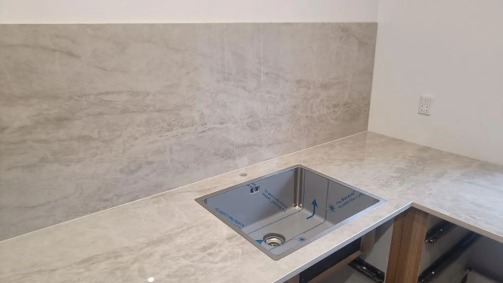 Underlimmad rostfri diskho monterad under en polerad köksbänkskiva i Dekton Arga keramik med stänkskydd i Glostrup.
