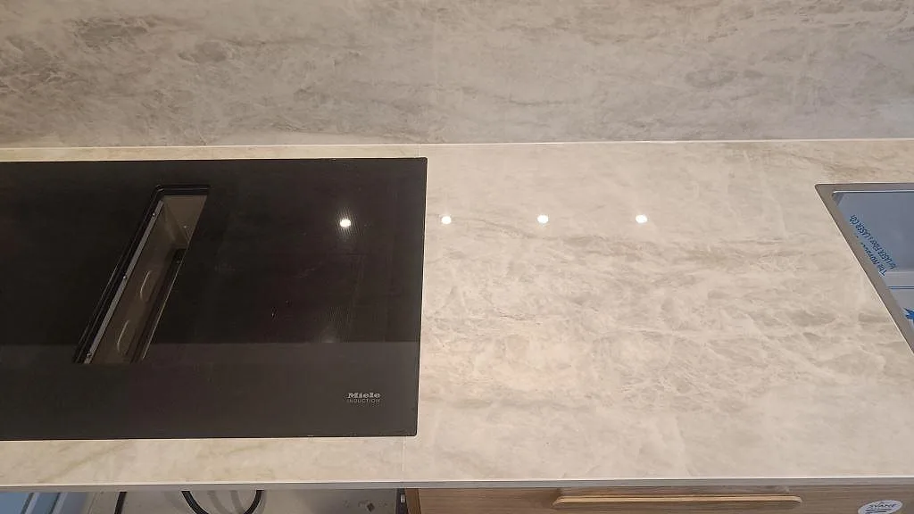 Polerad Dekton Arga mellan induktionshäll och diskho, med ljus ådring och speglingar i köket i Glostrup.