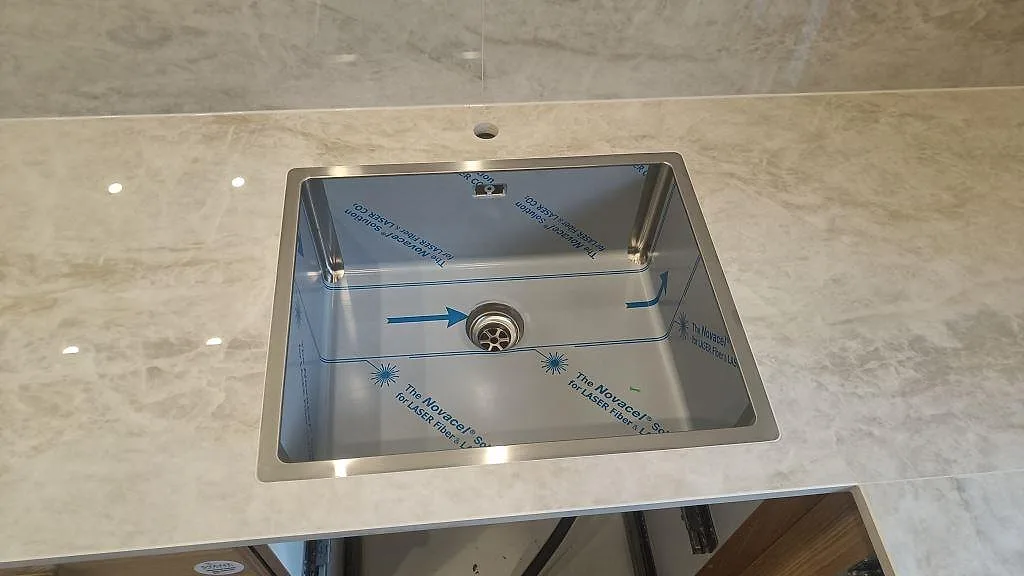 Närbild på underlimmad rostfri diskho och blandarhål i en polerad köksbänkskiva i Dekton Arga i Glostrup.