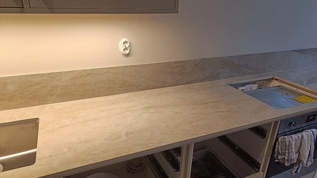 Lång köksbänkskiva i polerad Dekton Arga med hällöppning, diskho och 8 mm stänkskydd under montering i Göteborg.