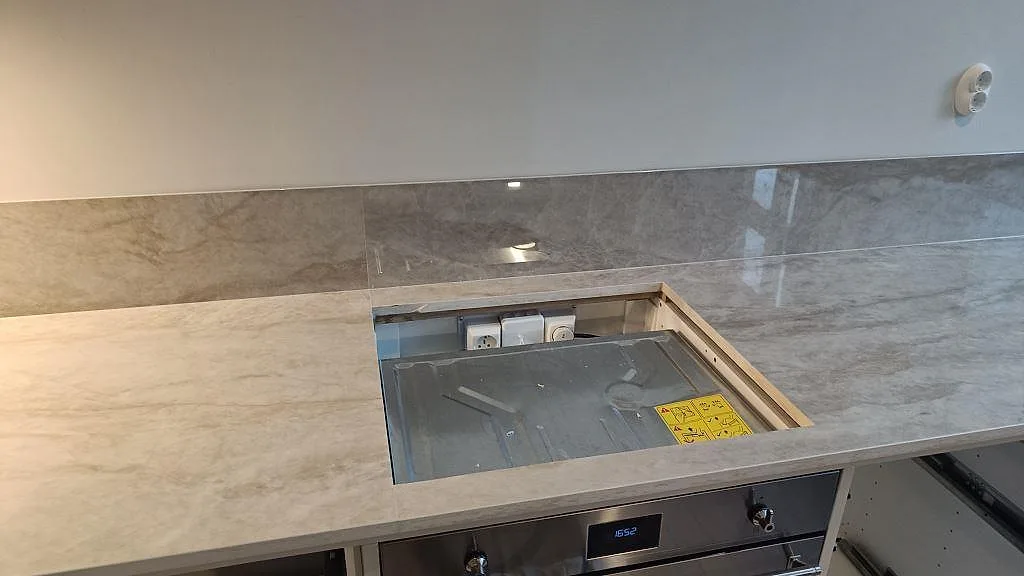 Detalj av polerad Dekton Arga runt hällöppningen med matchande stänkskydd i ett kök i Göteborg.