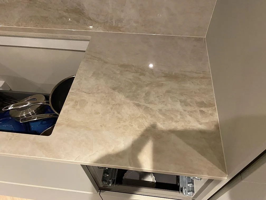 Höger arbetsyta i polerad Dekton Arga bredvid hällurtaget, med ådrad väggbeklädnad i ett kök i Greve.
