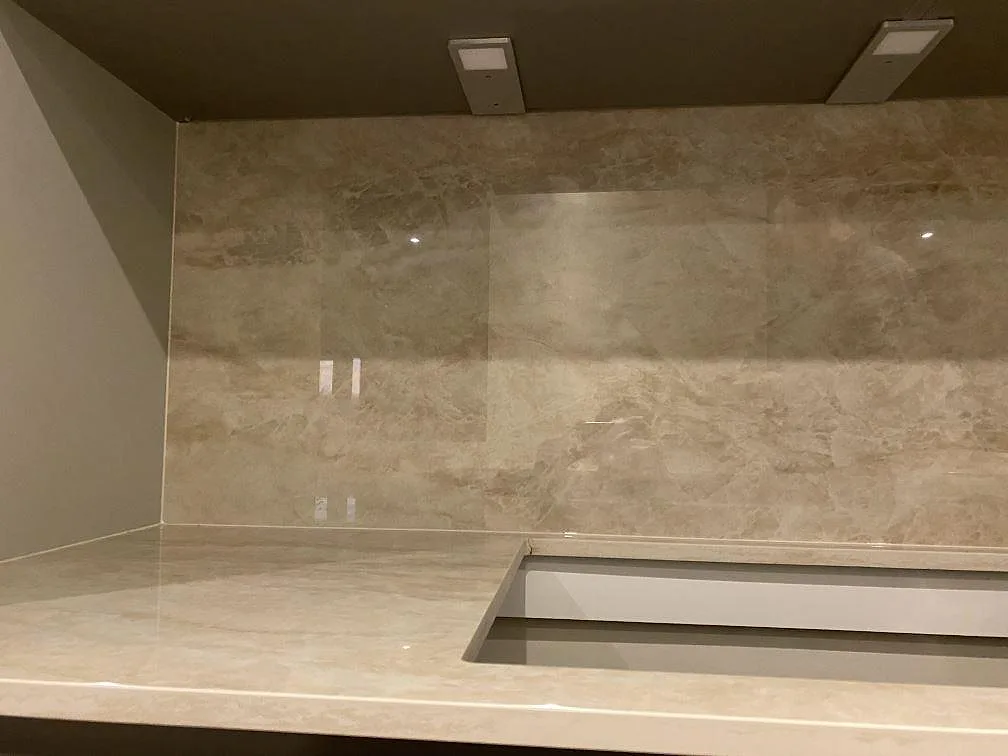 Närbild på polerad Dekton Arga som köksbänkskiva och väggbeklädnad med hällurtag under överskåp i Greve.