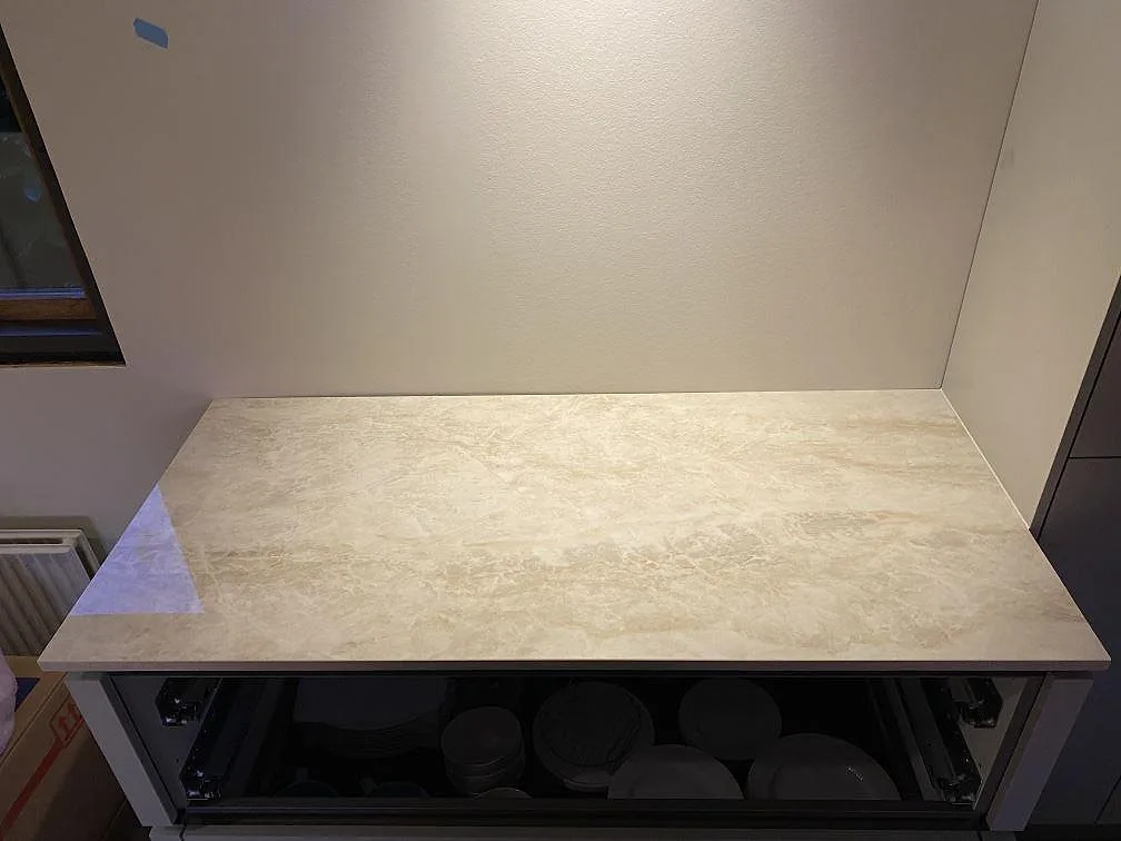 Separat bänkdel i polerad Dekton Arga med ljus beige ådring på öppen skåpstomme i ett kök i Greve.