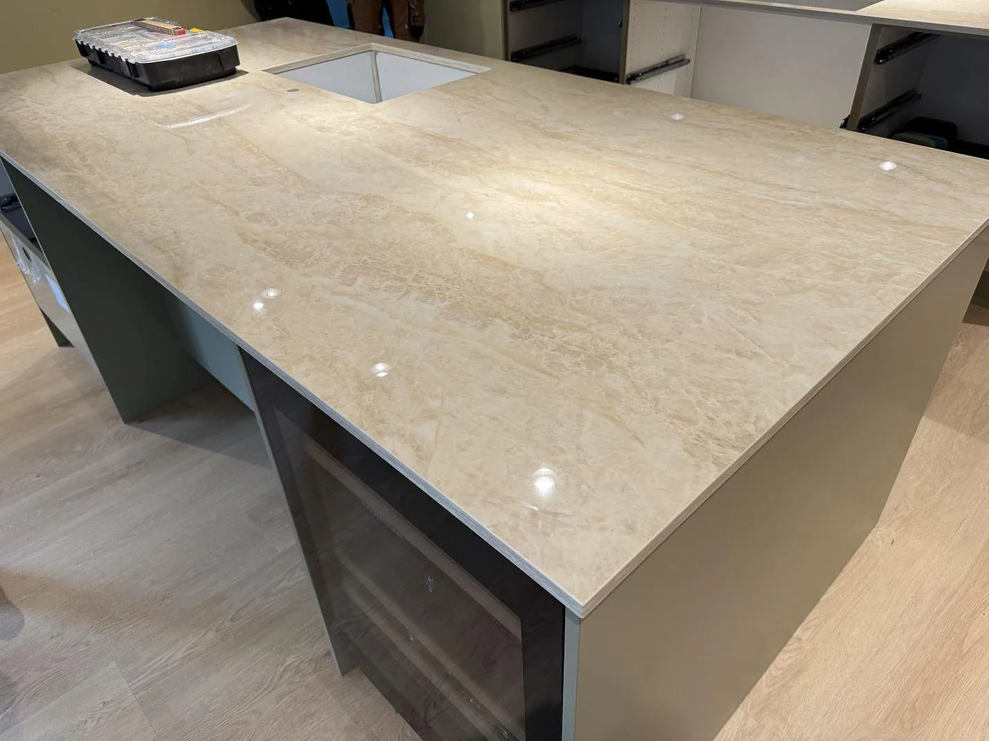 Köksö med polerad bänkskiva i Dekton Arga, cremebeige keramik med ljus ådring, och en rektangulär utskärning i ett kök i Greve.