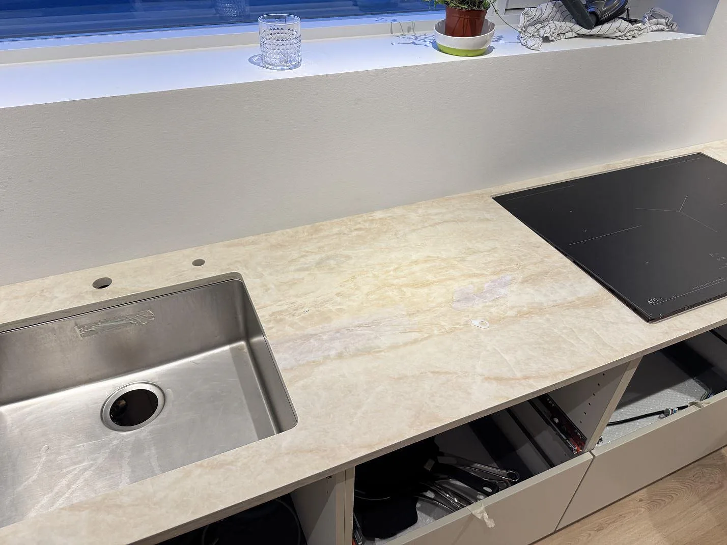 Köksbänkskiva i cremebeige Dekton Arga, 20 mm polerad, med infälld induktionshäll och underlimmad rostfri diskho i en lång rad i ett kök i Greve.