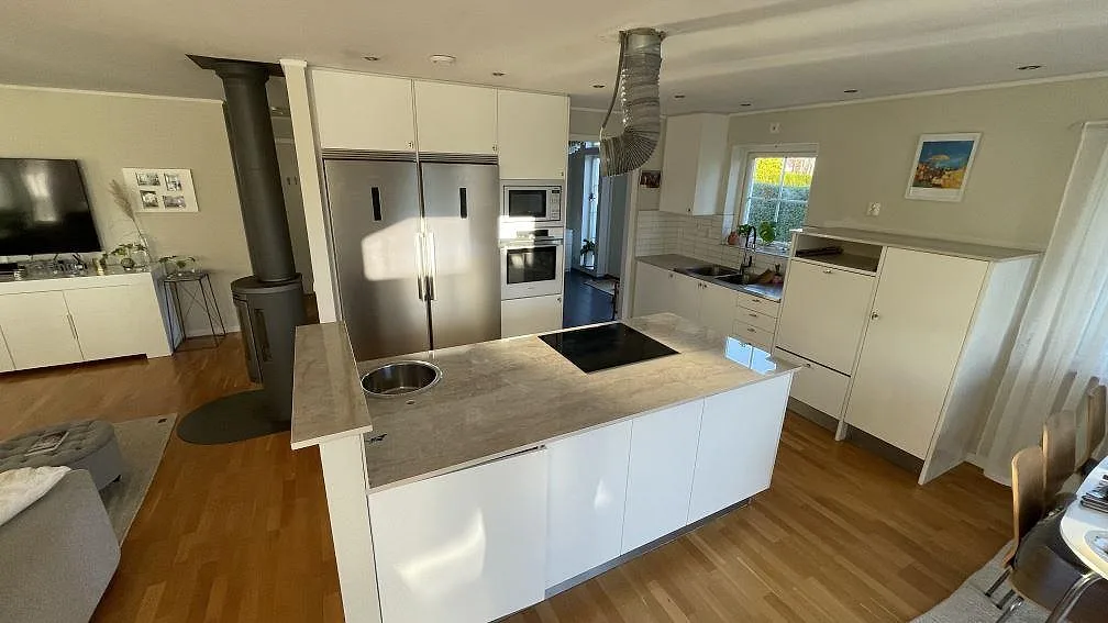 Köksbänkskiva i polerad Dekton Arga med köksö, rund rostfri diskho och svart häll i ett öppet kök i Hasslö.