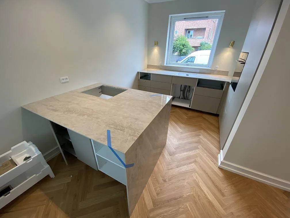 Köksbänkskiva i polerad Dekton Arga, 12 mm keramik, med fristående arbetsdel, vattenfallsida och rak diskbänk under fönster i Hellerup DK.