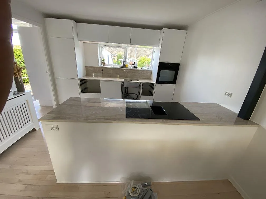 Köksbänkskiva och köksö i polerad Dekton Arga med svart häll, vitt kök och stänkskydd i Hillerød.