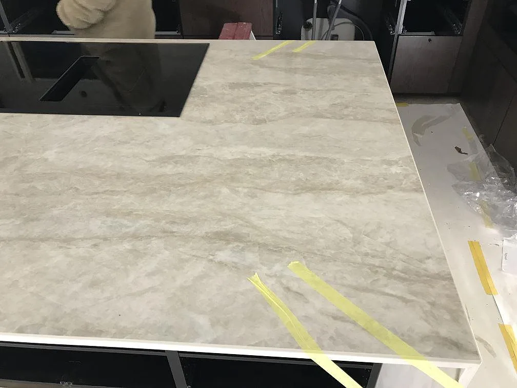 Köksö i varm krämvit Dekton Arga, polerad, med infälld induktionshäll under montering i ett kök i Höllviken.