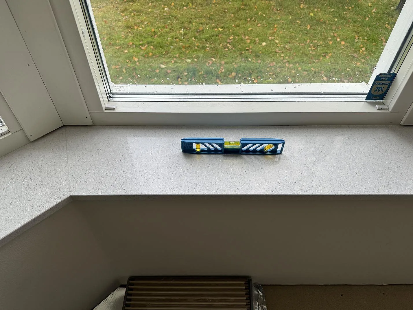 Rak fönsterbänk i polerad Dekton Arga med vattenpass framför fönster i Höllviken.