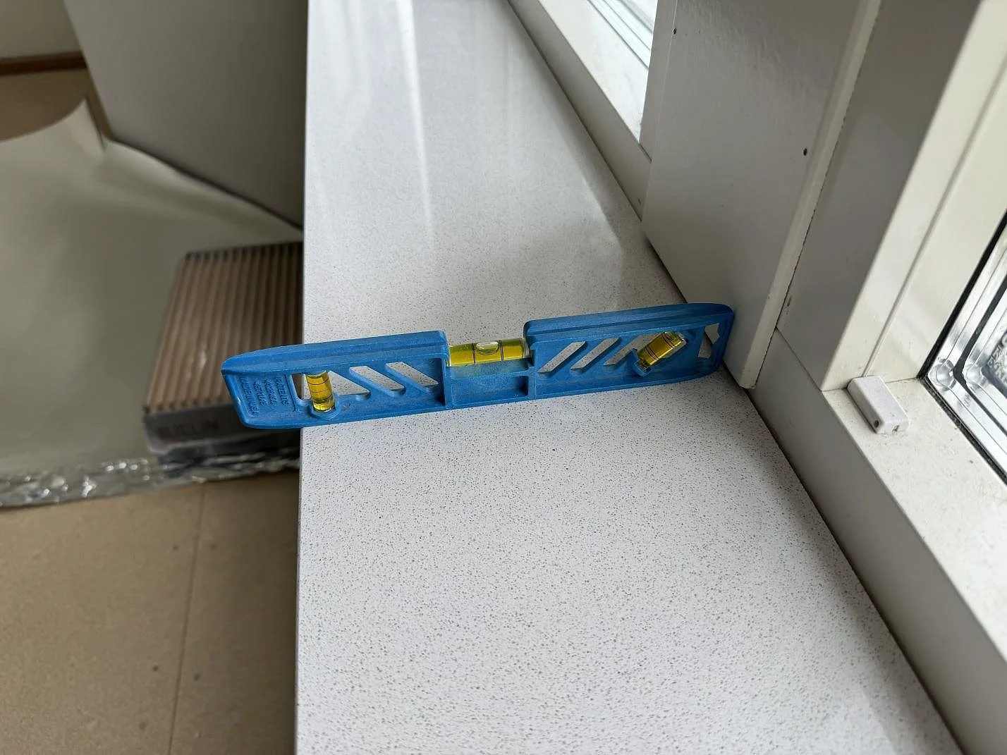 Närbild av polerad Dekton Arga som fönsterbänk med vattenpass vid fönsterkarm i Höllviken.