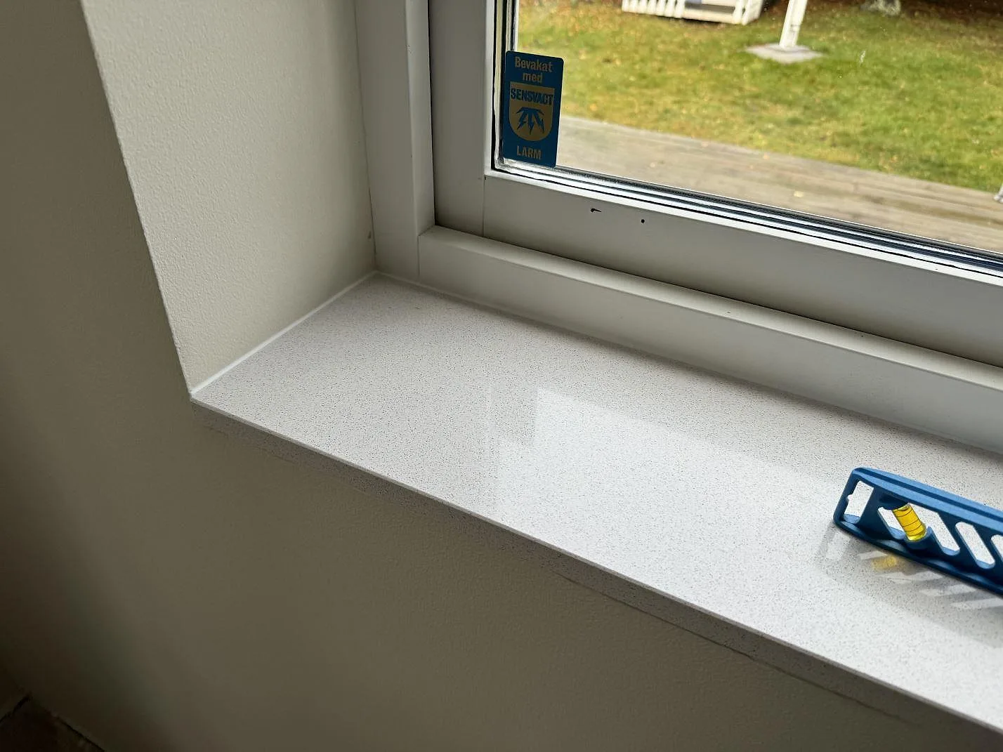 Detalj av polerad Dekton Arga fönsterbänk med ljus mönstring och vattenpass i Höllviken.