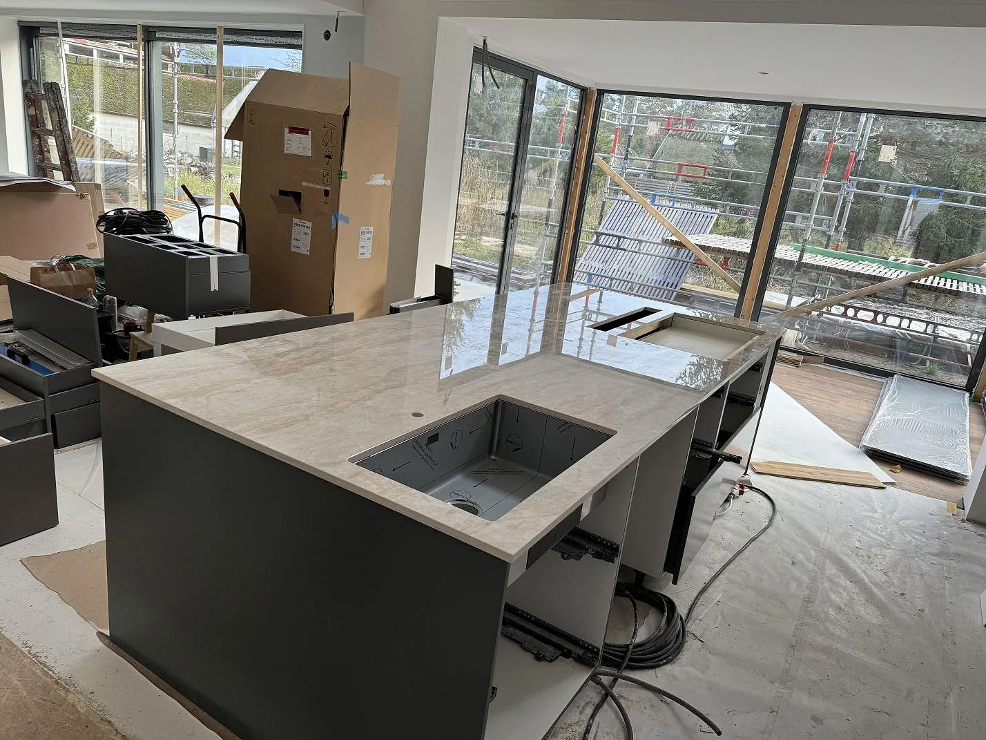 Stor köksö i polerad Dekton Arga, beige keramik med travertinlik ådring, monterad i ett kök under renovering i Höllviken.