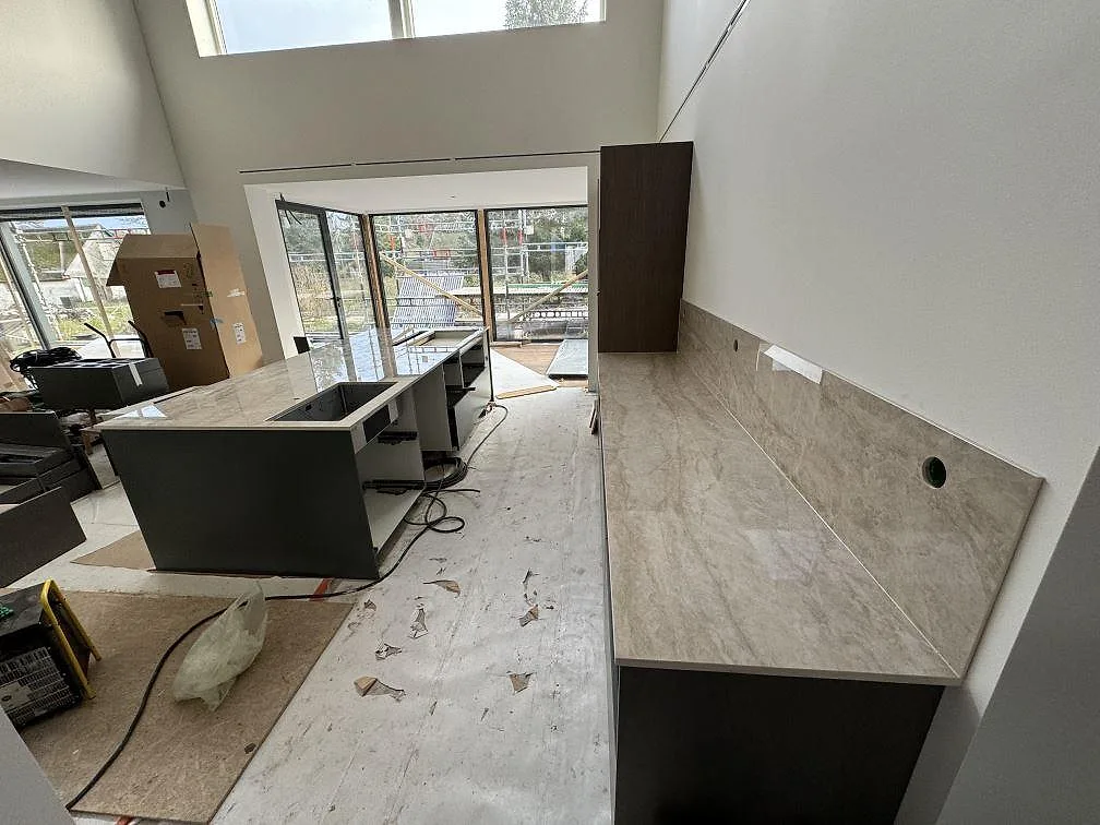 Översiktsbild av kök under montering med köksö, väggbänk och stänkskydd i polerad Dekton Arga i Höllviken.