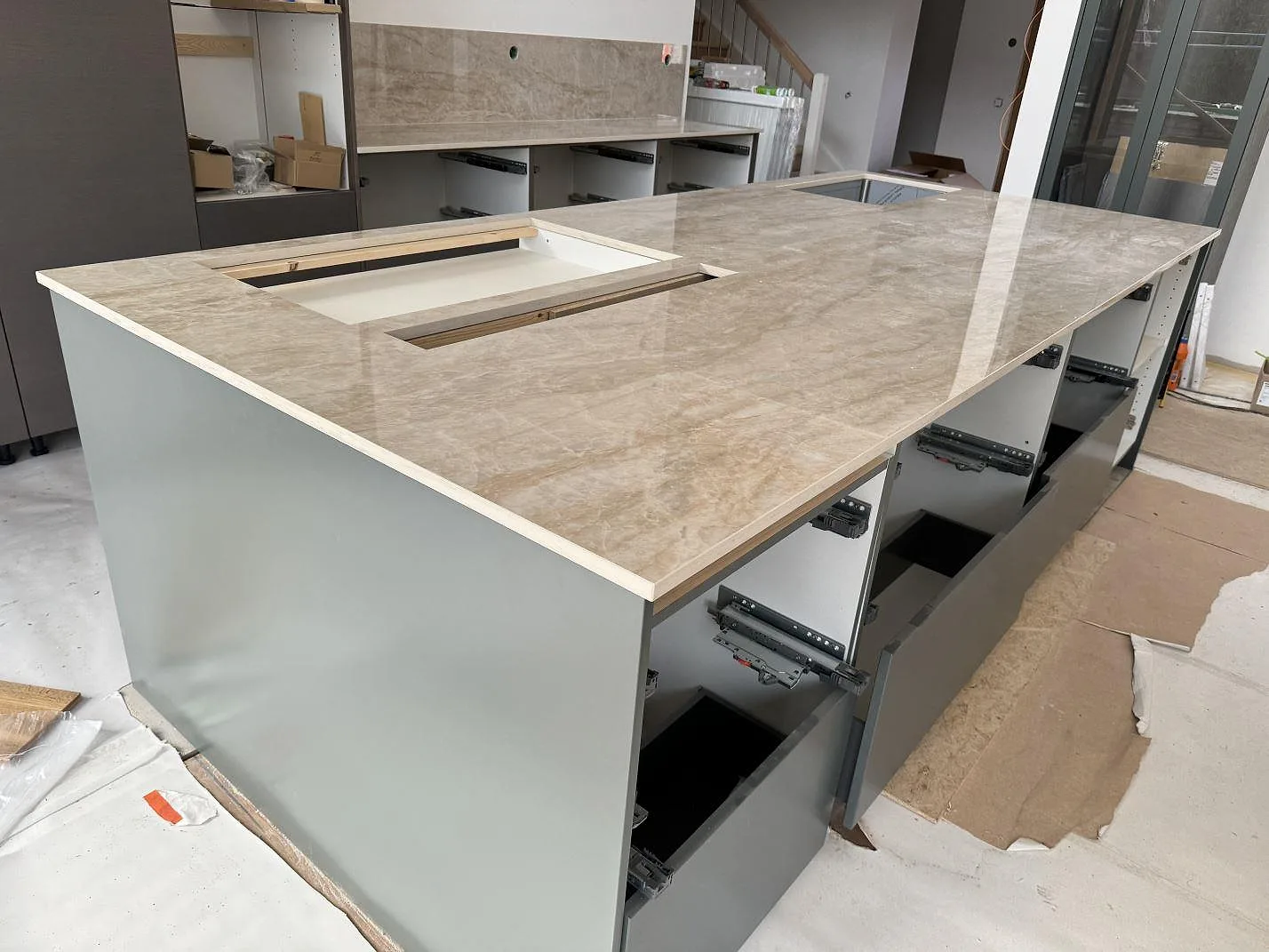 Polerad Dekton Arga på stor köksö med synliga urtag och öppna grå stommar under montering i Höllviken.