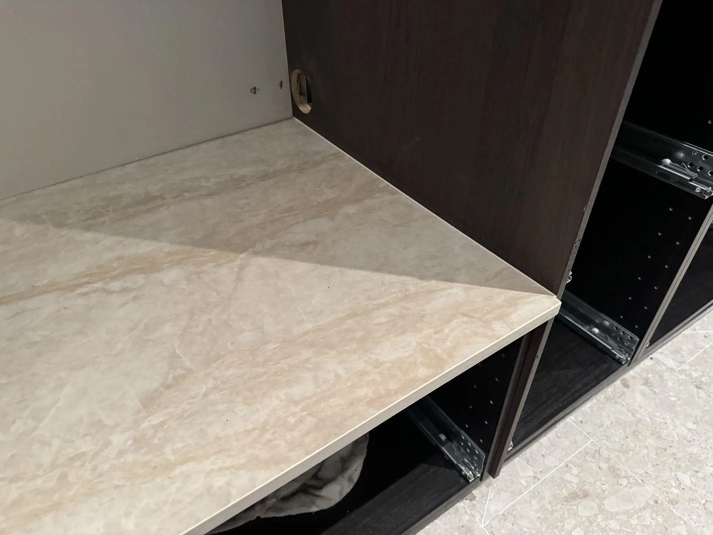 Hörnparti i kök med polerad Dekton Arga som bänkskiva, ljus stenyta och öppna mörkbruna stommar under montering i Höllviken.