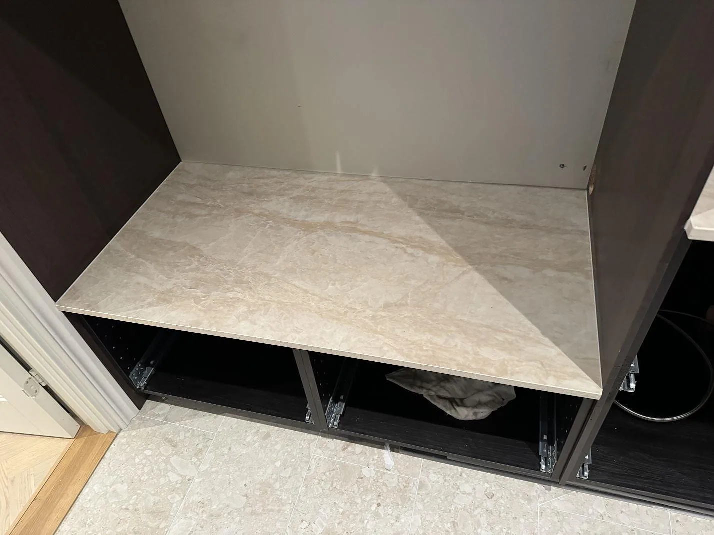 Installerad köksbänkskiva i polerad Dekton Arga mellan mörkbruna stommar, med stenens beige ådring synlig i Höllviken.